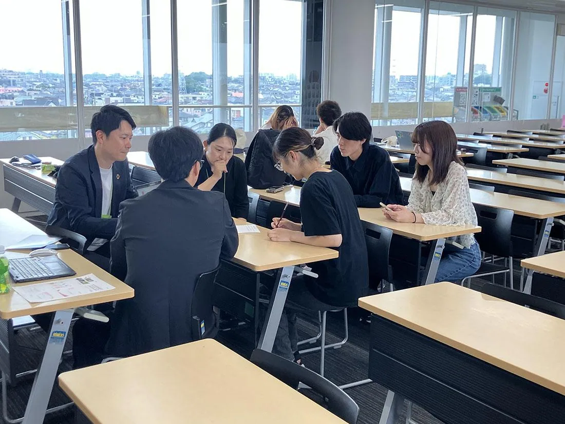 机を囲んで共同研究の意見交換をする学生と関係者